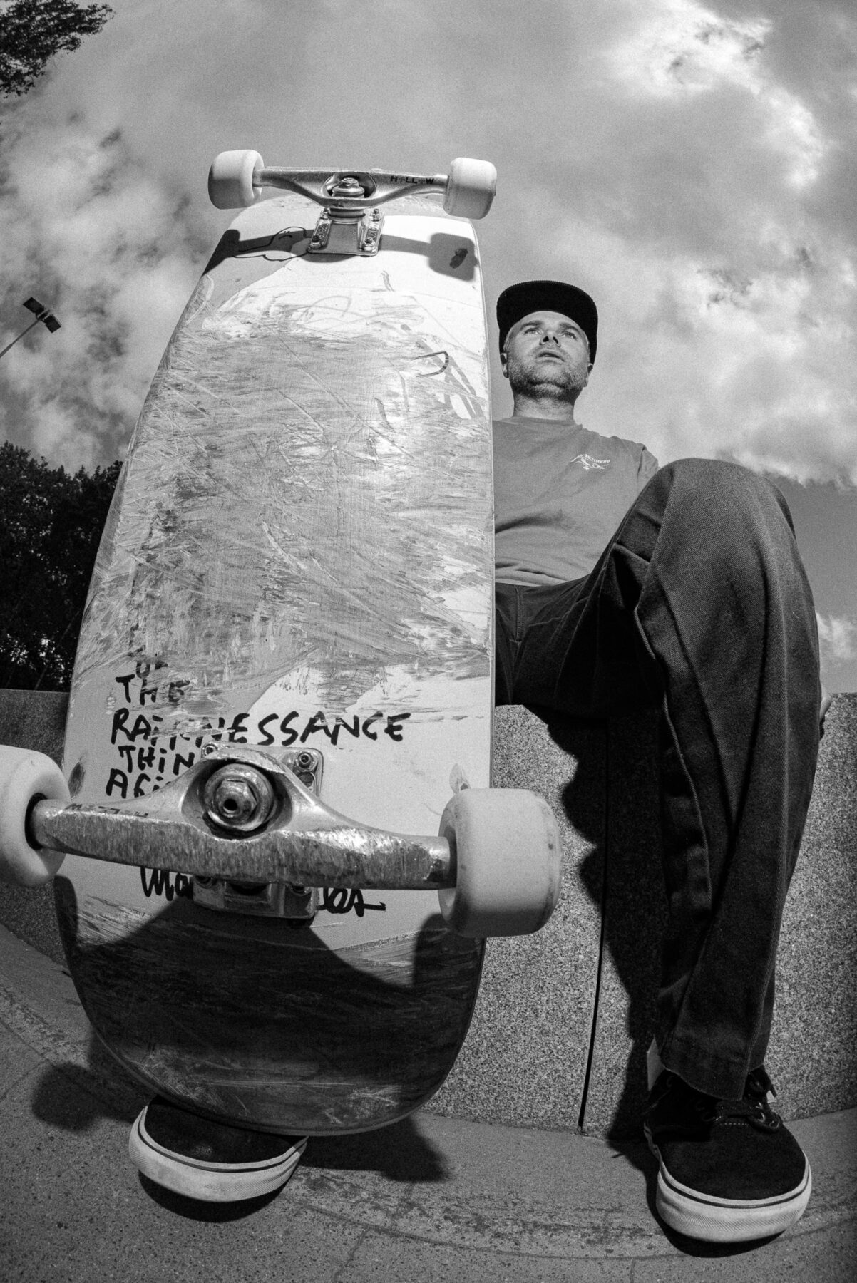 A fisheye photo of a person sitting with a skateboard in front focus.