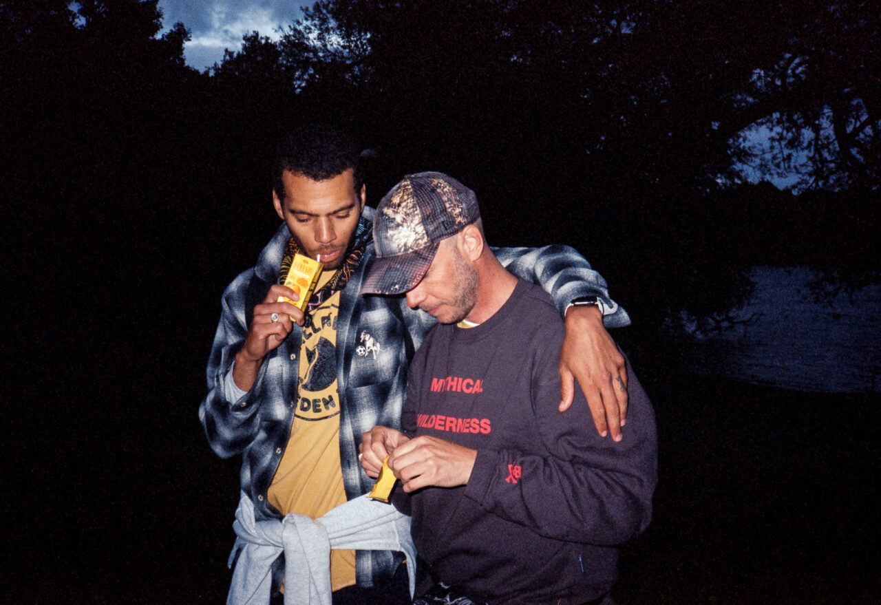 Two friends reloading a film camera and sipping on a juice box